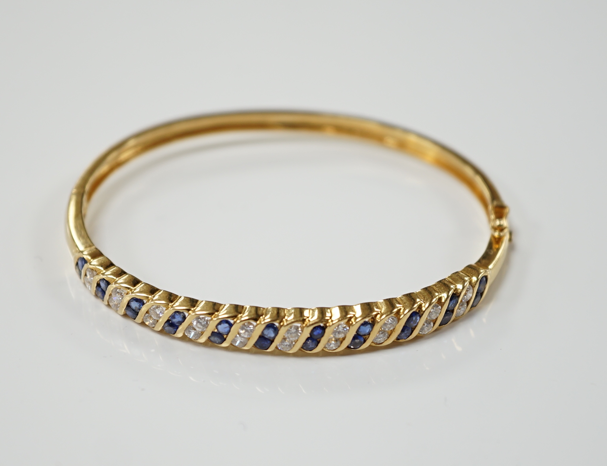 A 750 yellow metal, sapphire and diamond cluster set hinged bangle, interior diameter 56mm